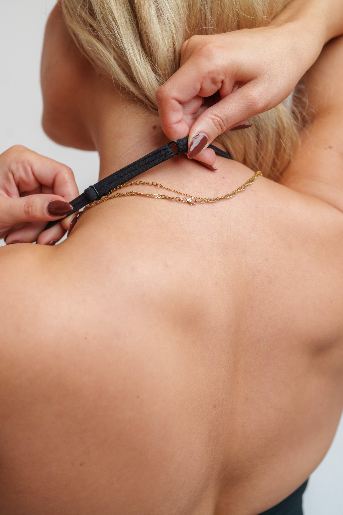 Person adjusting a black strap on a gold necklace worn by another person.